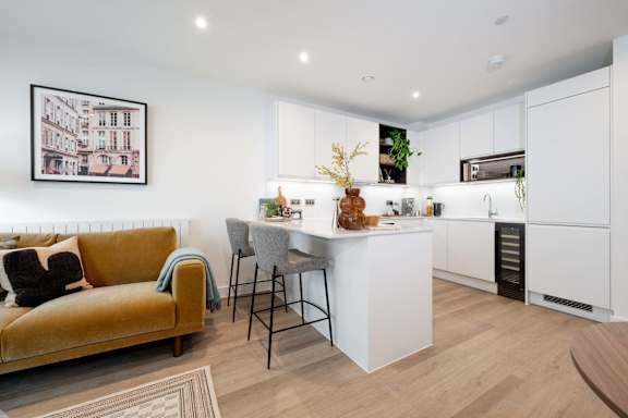 A modern kitchen with a yellow sofa and a framed picture on the wall.