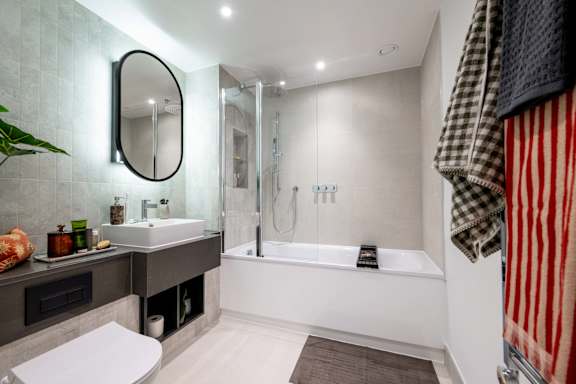 A modern bathroom with a white tub and a round mirror.