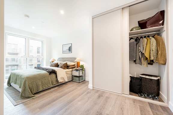 A bedroom with a large bed and a closet with clothes hanging.