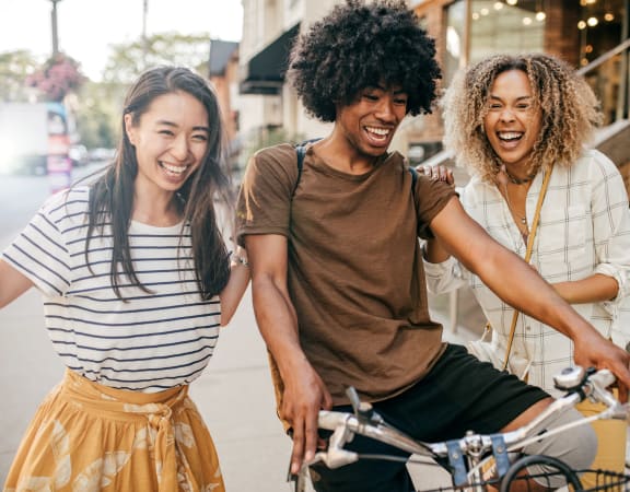 three young adults riding a bike on a city street