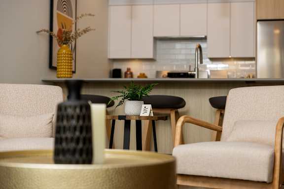 A modern living room with a white sofa, a wooden chair, and a coffee table with a black vase on it.