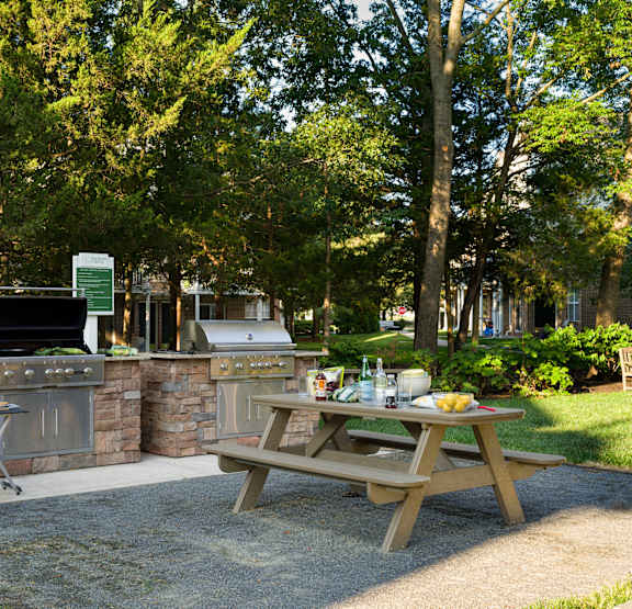 A picnic table is set up in front of a stone wall with a grill and a cooler.