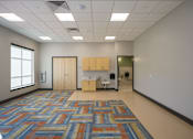 Thumbnail 1 of 7 - A room with a patterned carpet and a kitchenette.