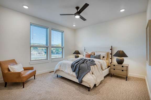 A bedroom with a bed, chair, and ceiling fan.
