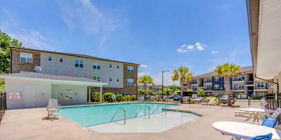 A swimming pool with a blue chair and a white table in front of a building.