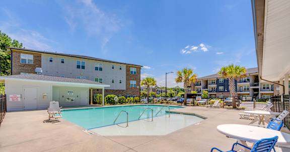 A swimming pool with a blue chair and a white table in front of a building.