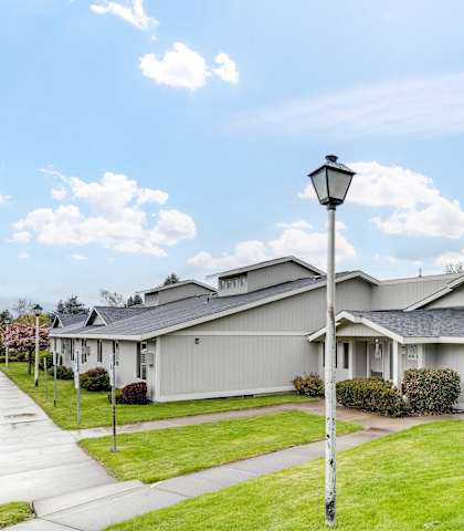 the view of a gray house with a yard and street light