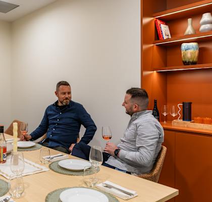three people sitting around a table drinking wine and watching tv