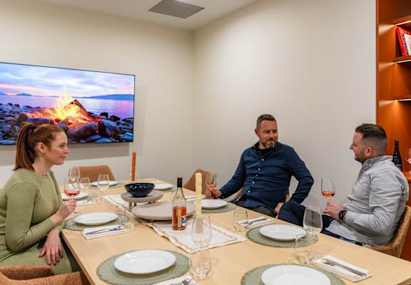 three people sitting around a table drinking wine and watching tv