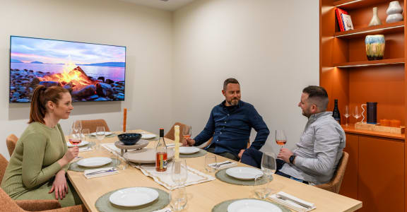 three people sitting around a table drinking wine and watching tv