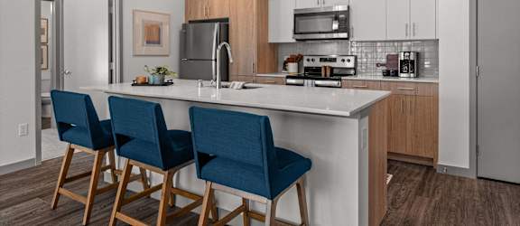 a kitchen with a large island with three blue chairs