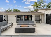 Thumbnail 5 of 6 - A modern house with a grey sofa and a fire pit in the front yard.