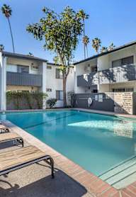 A pool with sun loungers in front of apartment buildings.