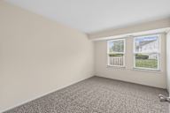 A room with a carpeted floor and a window showing a fence and trees outside.