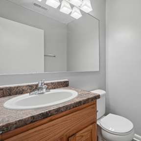 A bathroom with a toilet, sink, and mirror.