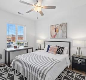 Apartment bedroom with desk, ceiling fan, and large window