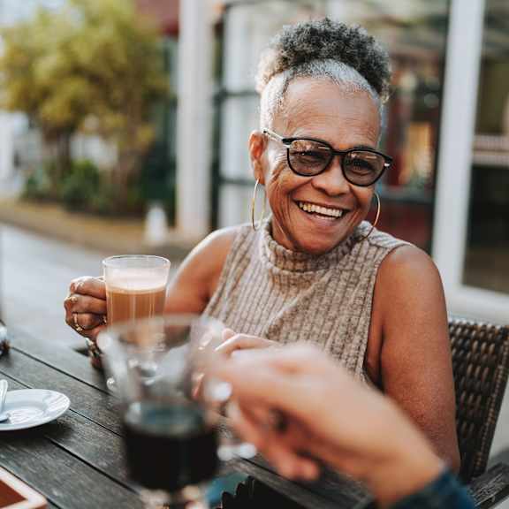A woman is sitting at a table with a glass of coffee in front of her.