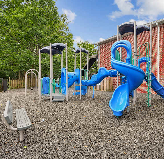 A playground with a blue slide and a grey bench.