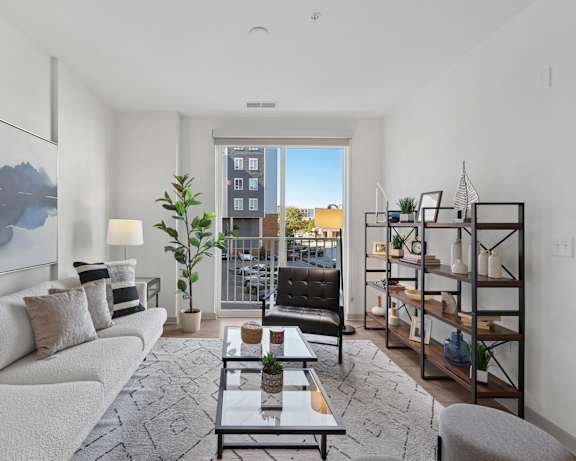 Apartment living room with sofa, accent chair, large windows, and open shelving