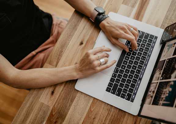 A person is typing on a laptop with a smartphone and tablet beside it.