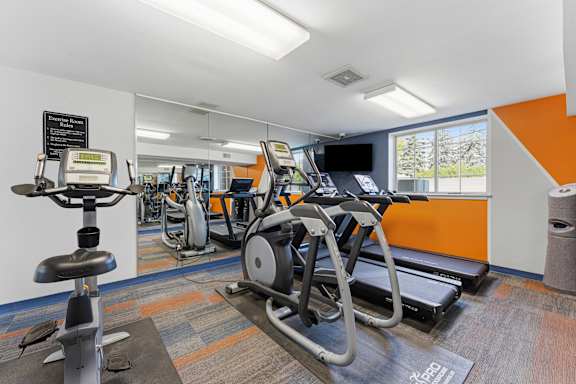 A gym with a row of treadmilers and elliptical machines.