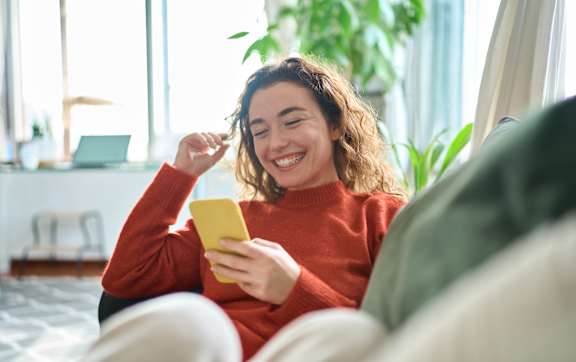 A person in a red top is sitting on a couch, holding a yellow object in their hands.