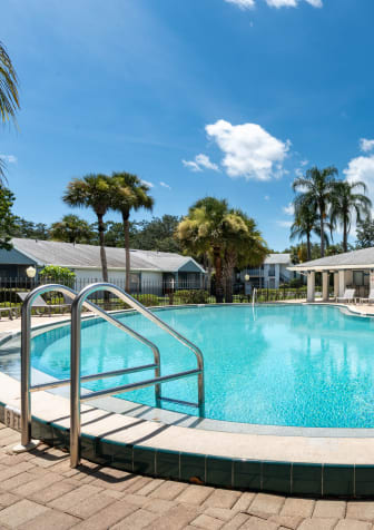 Large swimming pool with palm trees in the background at Aqua Bay Apartments in Naples, FL 34116