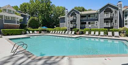 A swimming pool surrounded by lounge chairs in front of apartment buildings.