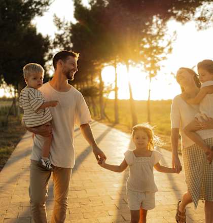 A family of four is walking together on a path during sunset.