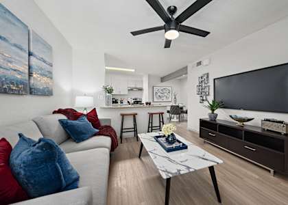 A modern living room with a grey sofa, a white coffee table, and a black ceiling fan.