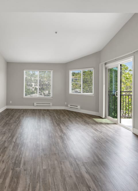 an empty living room with wood floors and a door to a balcony