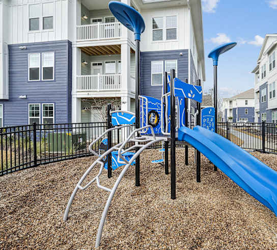 A playground with a blue slide and a black fence.