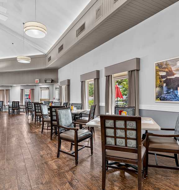 A living room with a grey sofa, a yellow chair, a wooden cabinet, a glass coffee table, and a ceiling fan. at King City Senior Village Apartments, King City, Oregon