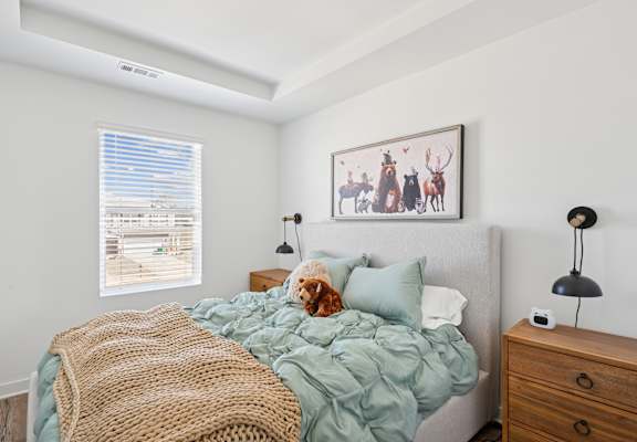 A bedroom with a bed, a blanket, a lamp, and a picture on the wall.