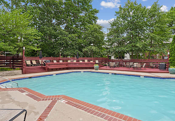 A large outdoor swimming pool surrounded by trees and a red fence.