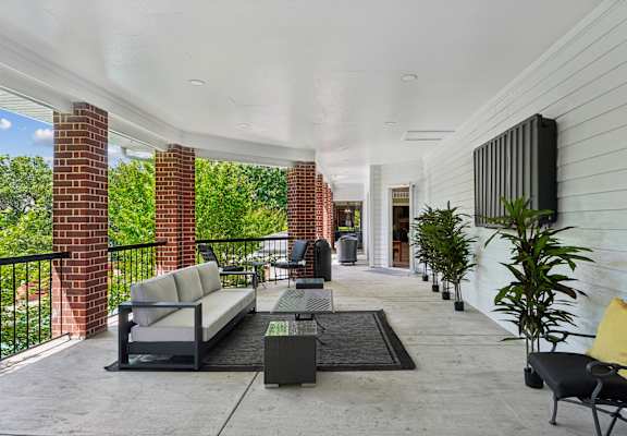 A patio with a black couch and a black chair with a yellow pillow.