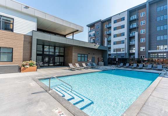 A swimming pool in front of a building with lounge chairs around it. at Cadence at Griesbach, Edmonton, AB