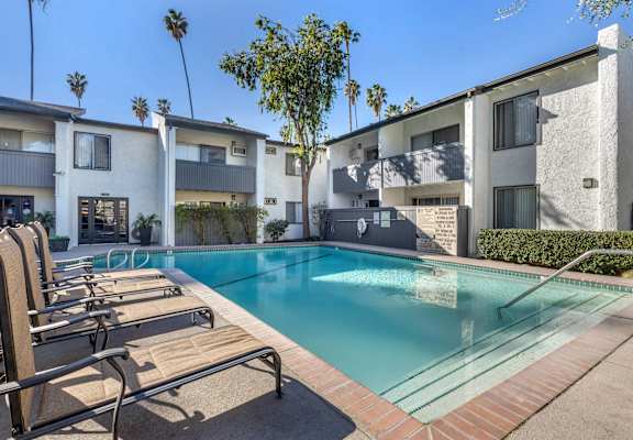 A pool with sun loungers in front of apartment buildings.