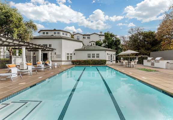 A large swimming pool in front of a white building with a patio area.