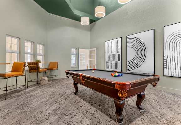 A pool table is in the middle of a room with chairs and artwork on the wall.