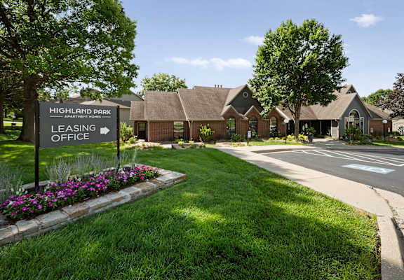 A sign for Highland Park Apartment Homes leasing office stands in front of a building.