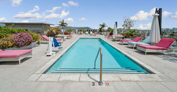 A swimming pool with a diving board and lounge chairs.