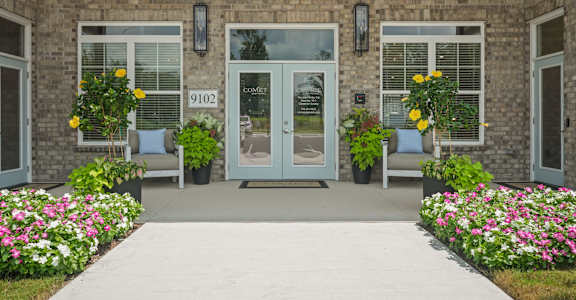 the front of a brick building with doors and a sidewalk with flowers