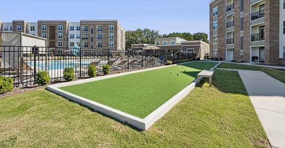 A grassy area in front of apartment buildings with a pool and a small pavilion.