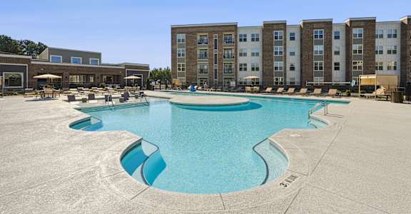 A large swimming pool in front of apartment buildings on a sunny day.