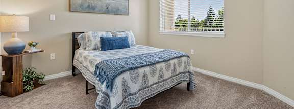 A bedroom with a bed, lamp, and painting on the wall.