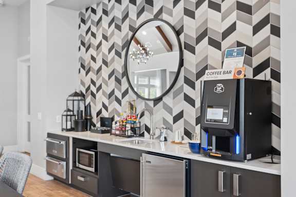 A coffee bar with a black and white chevron wallpaper and a mirror above it.
