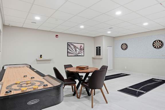 A room with a shuffleboard table and a dining table with chairs.