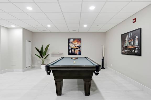 A pool table is in the middle of a room with a plant and pictures on the wall.