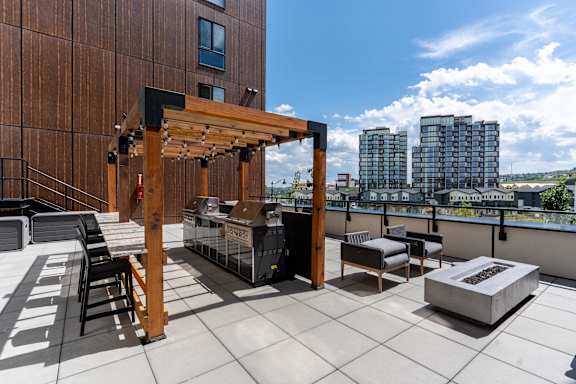 A wooden pergola is situated on a patio with black chairs and a grill.at Skyway Apartments, Calgary, AB T3B 5V6